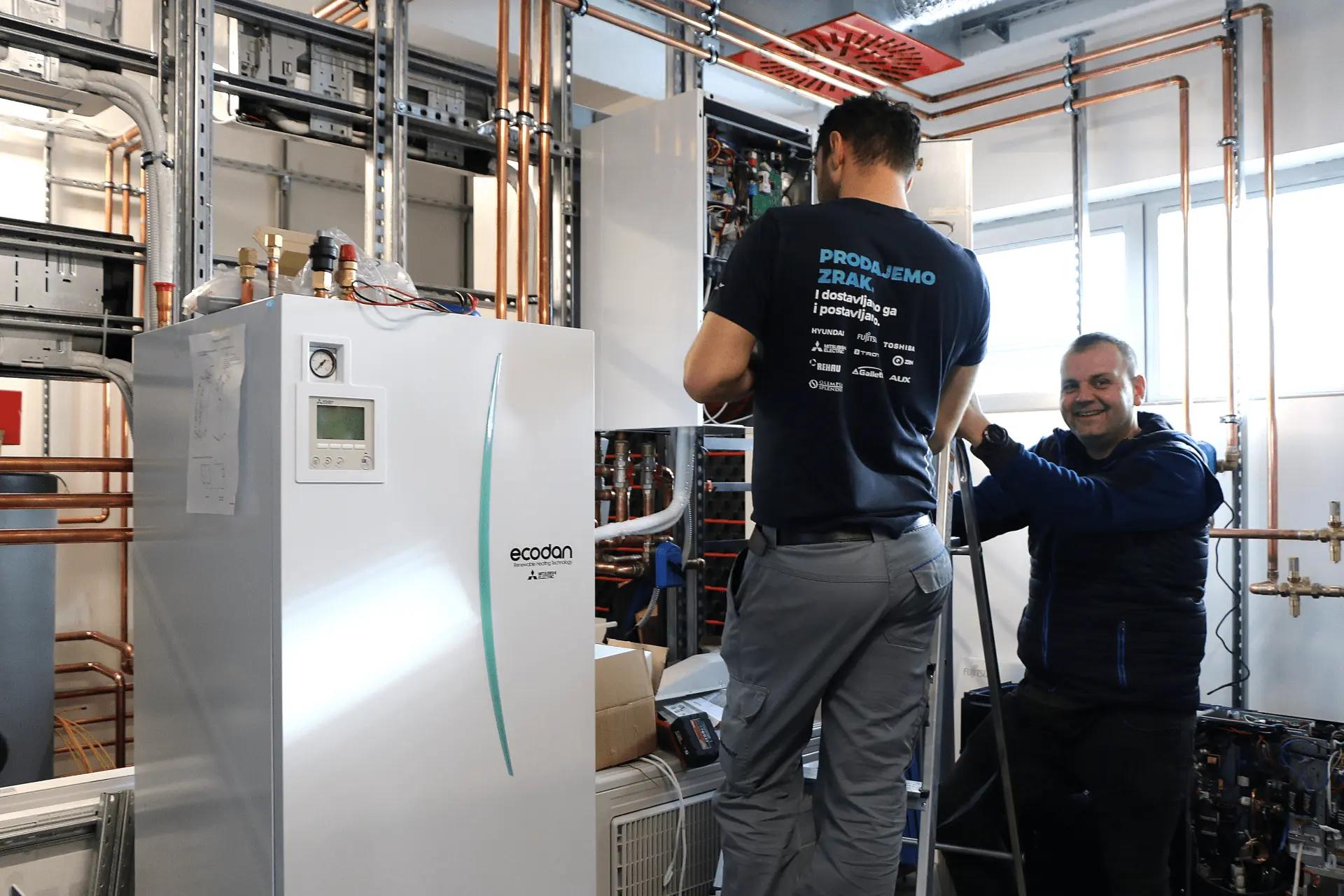 Dva instalatera rade na Mitsubishi Electric Ecodan dizalici topline u trening centru, uz bakrene cijevi i nosive profile